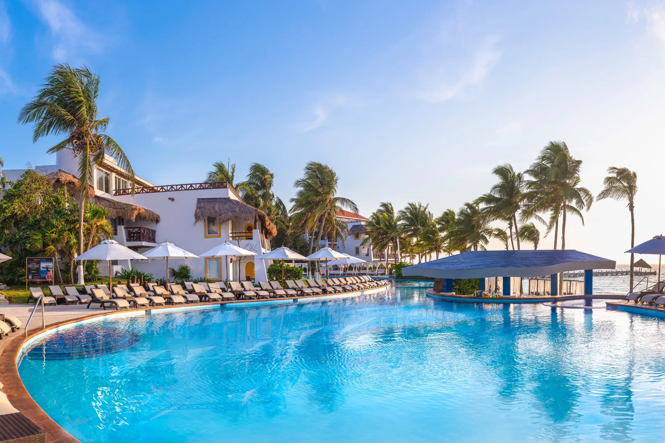 Oceanfront pool, palm trees, and resort buildings at Desire Riviera Maya Pearl Resort